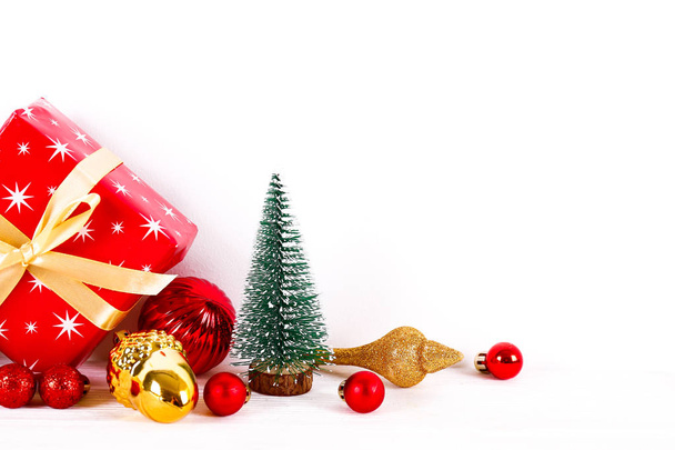 Minimalistic festive composition with small christmas tree, wrapped present and colorful matte balls. Fancy beautiful decoration for christmas pine tree. Background, copy space, close up, front view. - Photo, image