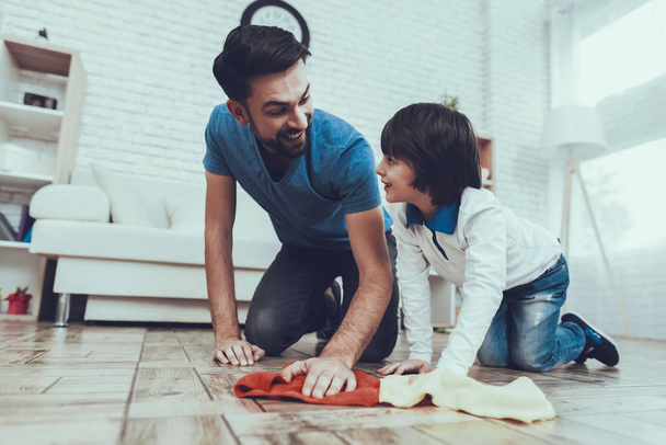 Man Spends Time with His Son. Father is Engaged in Raising Child. Father is Teaching a Son a Cleaning. Father and Son Washing the Floor with Rags. Persons is Smiling. People is Located in Bedroom. - 写真・画像