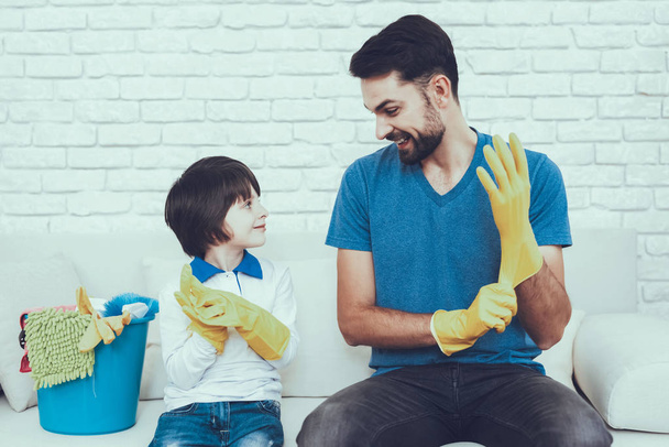 Man Spends Time with His Son. Father of Boy is Engaged in Raising Child. Father is Teaching a Son a Cleaning. Persons Weating a Gloves. Persons is Sitting on Couch. People is Located in Bedroom. - Foto, Imagem