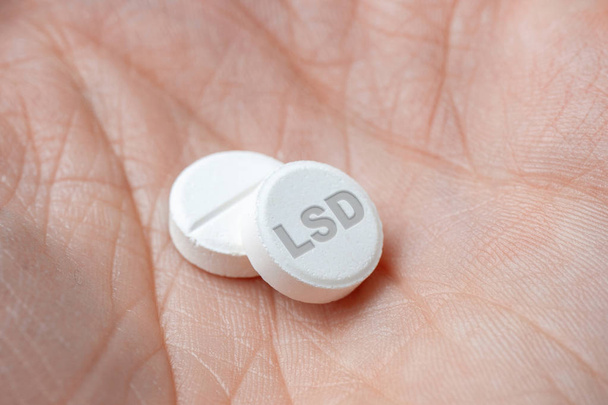 Две белые таблетки ЛСД в руке. Крупный план
 - Фото, изображение