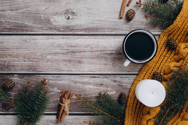 Cup of coffee  , candle, bumps, cinnamon, spruce branches and warm orange scarf on wooden table. Winter concept. Flat lay, top view.  - Foto, Imagen
