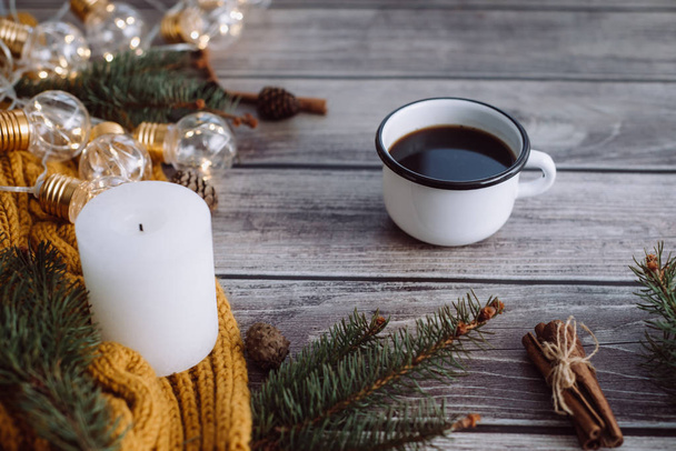 Cup of coffee  , candle, bumps, cinnamon, spruce branches and warm orange scarf and decorated with led lights  on wooden table. Winter concept. Flat lay, top view.  - Φωτογραφία, εικόνα