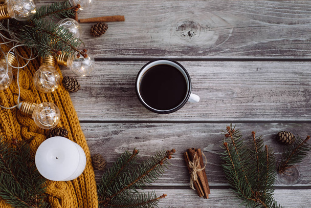 Cup of coffee  , candle, bumps, cinnamon, spruce branches and warm orange scarf and decorated with led lights  on wooden table. Winter concept. Flat lay, top view.  - Foto, immagini