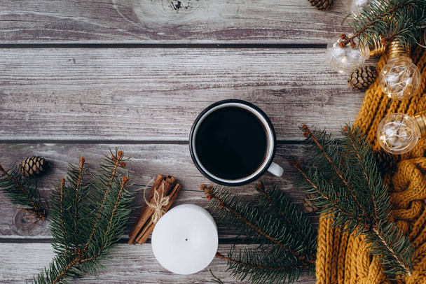 Cup of coffee  , candle, bumps, cinnamon, spruce branches and warm orange scarf and decorated with led lights  on wooden table. Winter concept. Flat lay, top view.  - Foto, Imagem