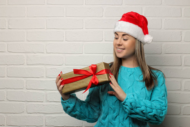 Emotional girl in a Santa Claus hat with Christmas gifts in their hands on a light background - Fotoğraf, Görsel