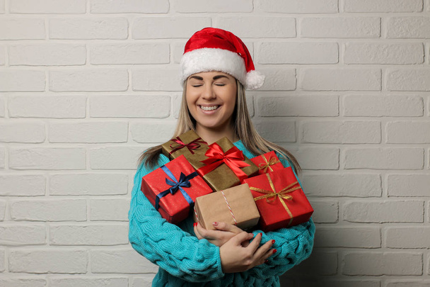 Emotional girl in a Santa Claus hat with Christmas gifts in their hands on a light background - Photo, Image