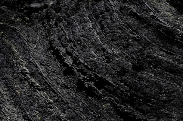 Zwarte ruwe rots textuur in het zonlicht en schaduw - Foto, afbeelding