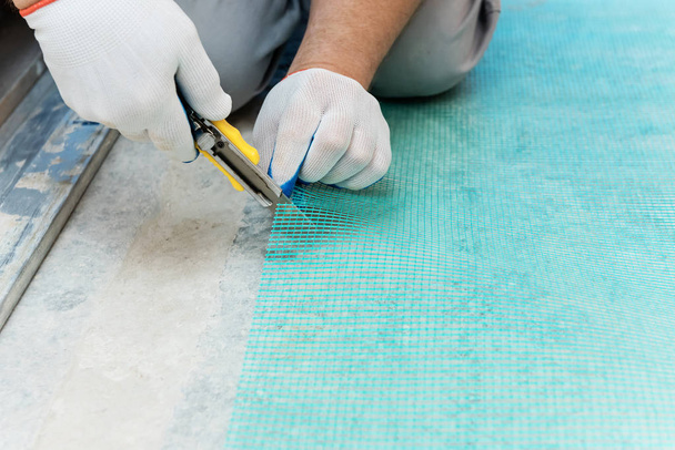 Un travailleur coupe un morceau de maille de fibre de verre avec un couteau
. - Photo, image