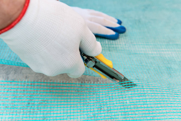 Um trabalhador está cortando um pedaço de malha de fibra de vidro com uma faca
. - Foto, Imagem