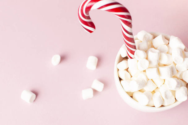 Bebida de Natal Ano Novo, caneca branca com marshmallows e Candy Cane na neve em fundo rosa Flat Lay espaço de cópia. Comida de bebida tradicional de inverno. Celebração da decoração festiva Férias de Natal 2019
 - Foto, Imagem