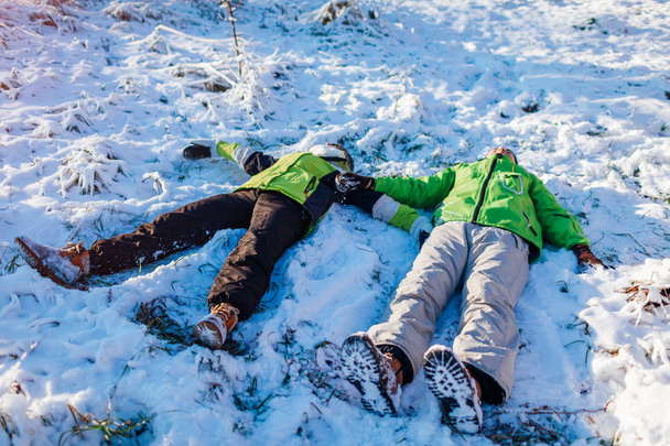 junges verliebtes Paar, das im Schnee liegt und Schnee-Engel bastelt. fröhliche Menschen, die Spaß im Winterwald haben. Saisonale Aktivitäten - Foto, Bild