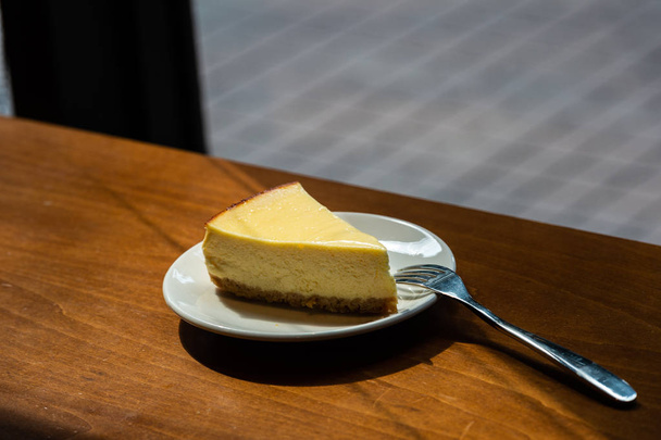 Plak New York Cheesecake op witte plaat op houten ondergrond - Foto, afbeelding