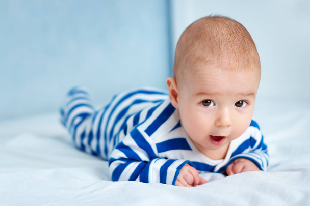 happy little boy lying in the bed. Funny four month old baby in striped sleepsuit at home. - Photo, Image