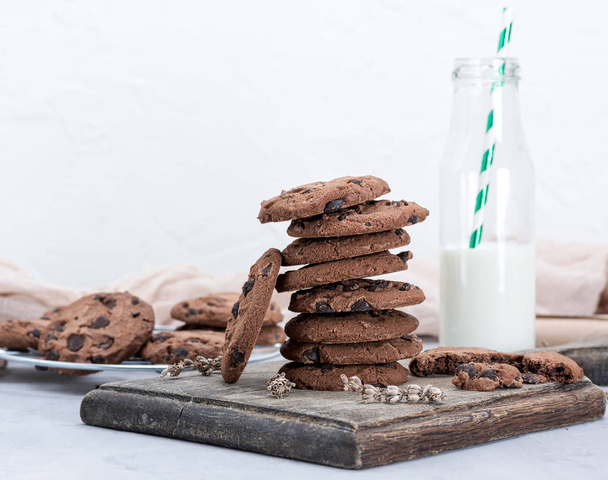 stack of round chocolate chip cookies and a glass bottle with milk on a brown wooden board - Foto, immagini