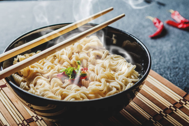 Μαύρο μπολ της Ασίας στιγμιαία noodles με ζεστό νερό και κόκκινες πιπεριές τσίλι και φρέσκο κρεμμυδάκι - Φωτογραφία, εικόνα