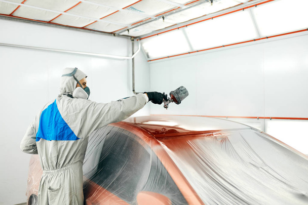auto painter in protective workwear and respirator painting car body in paint chamber - 写真・画像
