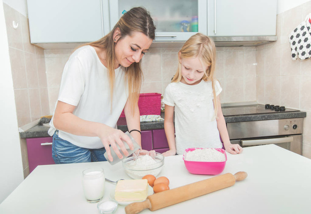 Счастливая семья веселится на кухне. Мама и ее дочь смешивают тесто дома
. - Фото, изображение
