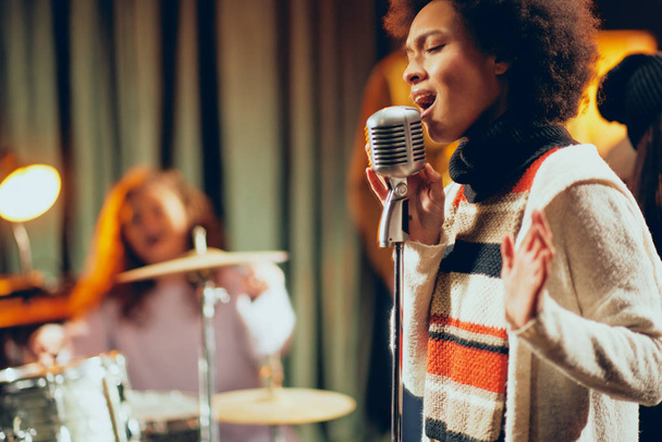 混血女性が歌うをクローズ アップ。背景バンドで楽器を演奏します。ホーム スタジオのインテリア. - 写真・画像