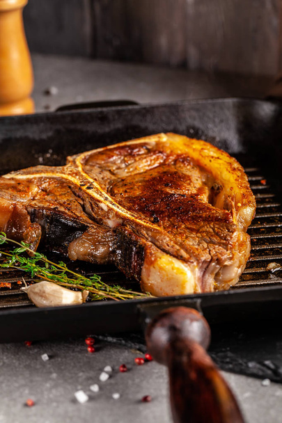 American cuisine. The concept of pral cooking meat. A fried piece of T-bone steak lies in a grill pan with peccias, thyme, and garlic. - Foto, Imagem