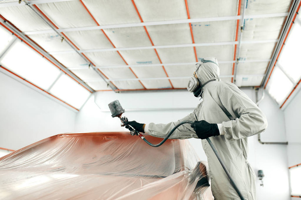 auto painter in protective workwear and respirator painting car body in paint chamber - Φωτογραφία, εικόνα