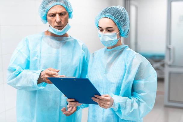Two doctors looking at the clipboard while standing in the corridor - Foto, Imagen