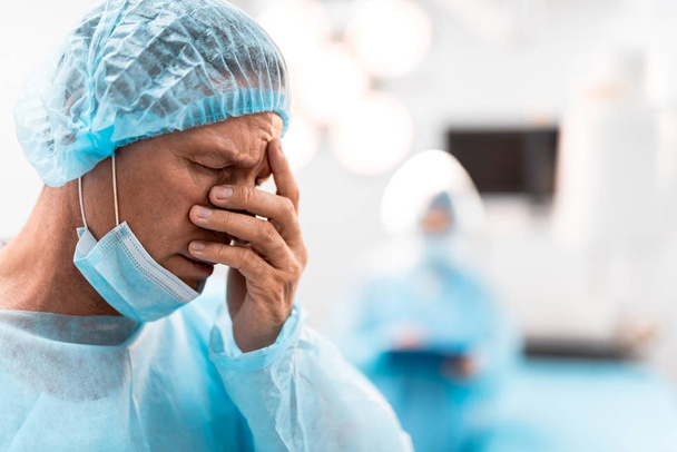 Sad doctor hiding his face after having tiresome surgery - Foto, Imagen