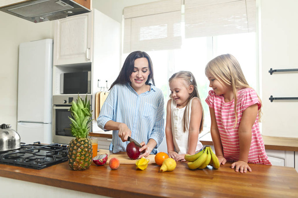 Девочки с мамой на кухне готовят свежий фруктовый салат
  - Фото, изображение