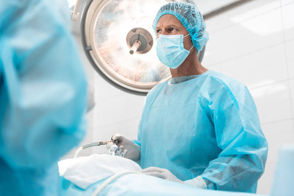 Serious surgeon frowning while standing in the operating theatre - Foto, afbeelding