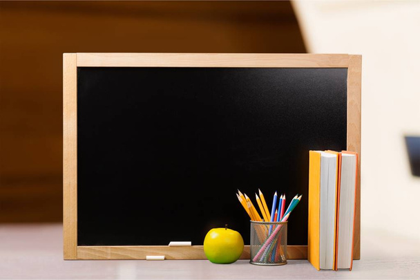 Stack of books, pencils and apple against blackboard, education and learning background - Фото, зображення