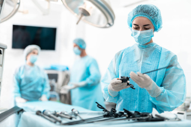 Jovem enfermeira de vestido azul segurando instrumento laparoscópico
 - Foto, Imagem