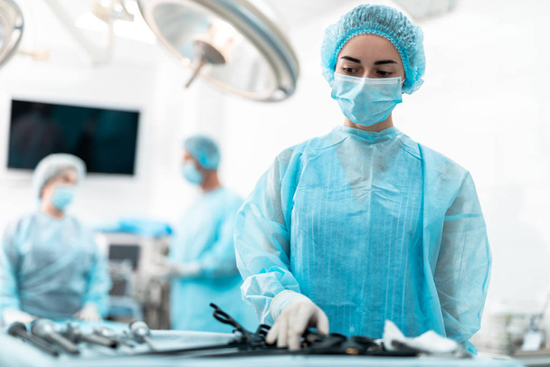 Young nurse in blue gown standing near table with laparoscopic tools - Foto, Bild