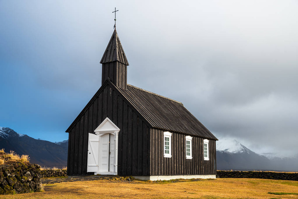 Eglise en bois noir avec de belles montagnes enneigées en arrière-plan en Islande un jour d'automne nuageux
 - Photo, image