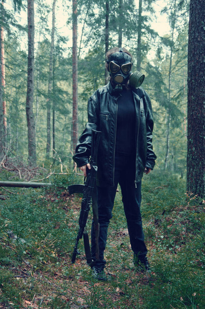 γυναίκα, σε μαύρο χρώμα με μια μάσκα αερίων στο κεφάλι της και ένα αυτόματο τουφέκι viciously περιπλανιέται μέσα από το δάσος σε αναζήτηση των αθώων θυμάτων που διψούν για αίμα - Φωτογραφία, εικόνα