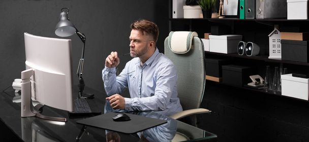 Ділова людина сидить в офісі за комп'ютерним столом і тримає рот дужки окулярів
 - Фото, зображення