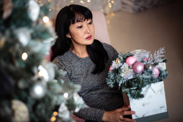 Adult woman florist makes a christmas winter composition over cozy home background - Photo, Image