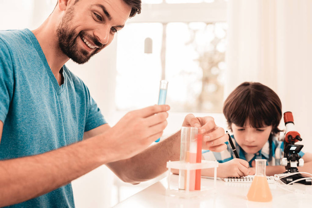 Youn Bearded Father Teaching Son in Shirt at Home. Education at Home. Using Microscope. Studding Chemistry. White Table in Room. Sitting Boy. Young Father. Lesson at Home. Education Concept. - Foto, immagini