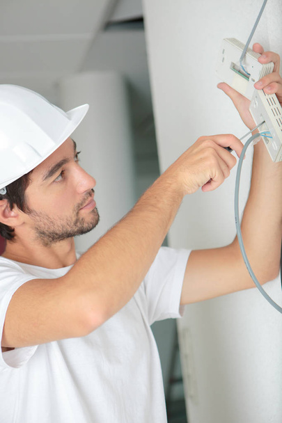 young electrician installing electrical device on wall - Zdjęcie, obraz