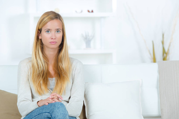 smutne, młodą kobietę, siedzącą przy kanapie w domu - Zdjęcie, obraz