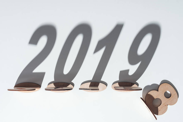 Ansicht von Holzzahlen mit Schatten auf weißem Hintergrund, die den Wandel von 2018 auf 2019 symbolisieren - Foto, Bild