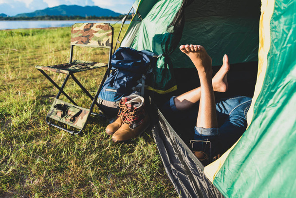 女性の足のテント キャンプでリラックスのクローズ アップ山湖と草原と草のフィールドの背景を持つ。ライフ スタイルと人々 の概念。キャンプと picnec のテーマ。緑の自然と夏の旅行のテーマ - 写真・画像