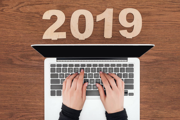 cropped view of woman using laptop at wooden table with 2019 date made of plywood - Photo, Image