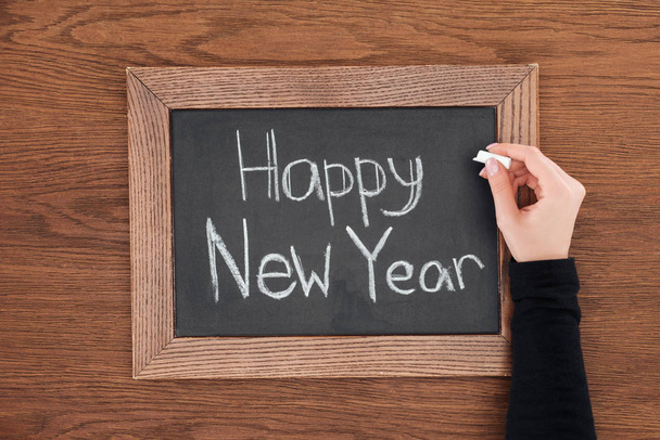 vista parcial de la mujer escribiendo 'feliz año nuevo' texto en pizarra con fondo de madera
 - Foto, Imagen