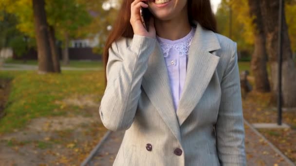 Nuori kaunis nainen puhuu matkapuhelimella puistossa, onnellinen tyttö hymyilee. kaunis liike nainen kuljettaa kädessään musta salkku asiakirjoja
. - Materiaali, video