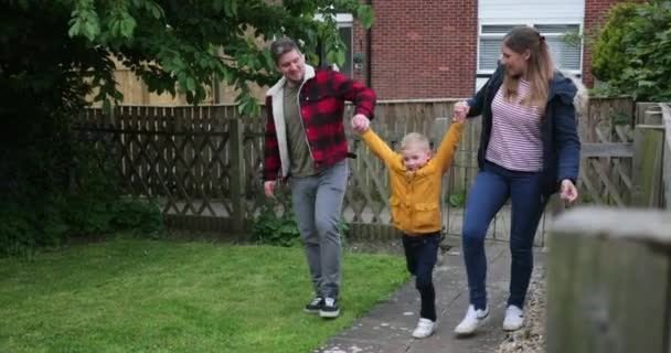 Mum and dad swinging their little boy in the air by his arms while walking through their garden after being out shopping for groceries. - Кадри, відео