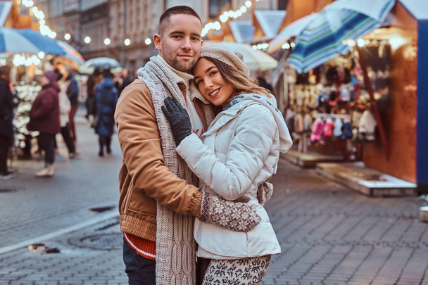 Un jeune couple romantique portant des vêtements chauds étreignant en plein air dans la rue du soir au moment de Noël, profitant de passer du temps ensemble
. - Photo, image