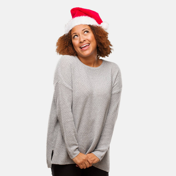 Young black woman wearing a santa hat dreaming of achieving goals and purposes - Foto, Bild
