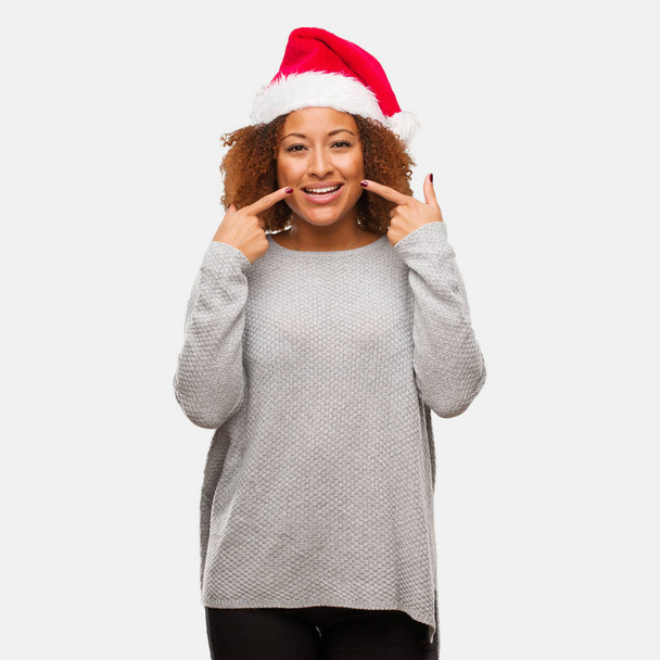 junge schwarze Frau mit Weihnachtsmütze lächelt und zeigt auf den Mund - Foto, Bild