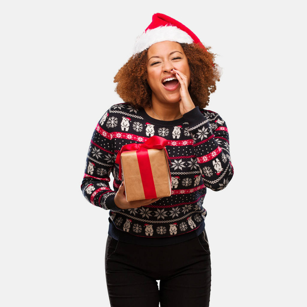 junge schwarze Frau hält an Weihnachten ein Geschenk in der Hand und schreit etwas Glückliches nach vorne - Foto, Bild