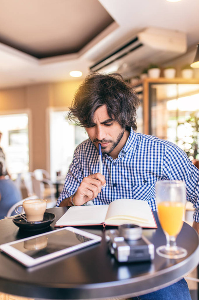 Jovem homem moderno tomando um café da manhã no café, escrevendo em um caderno, pensando em uma ótima ideia
. - Foto, Imagem