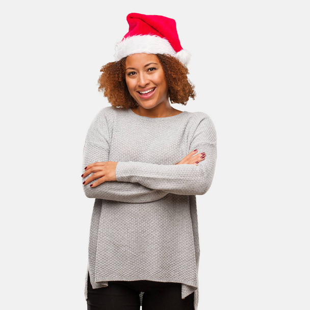 Mladá černá žena nosí klobouk santa přes ramena, s úsměvem a uvolněně - Fotografie, Obrázek